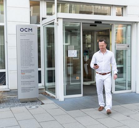 Arzt in weißer Kleidung vor der Eingangstür der OCM Praxis und Klinik