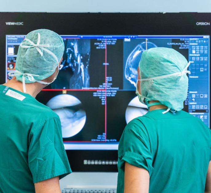 Zwei Ärzte in OP-Kleidung, Rückenansicht, Gespräch vor mehreren Röntgenbildern