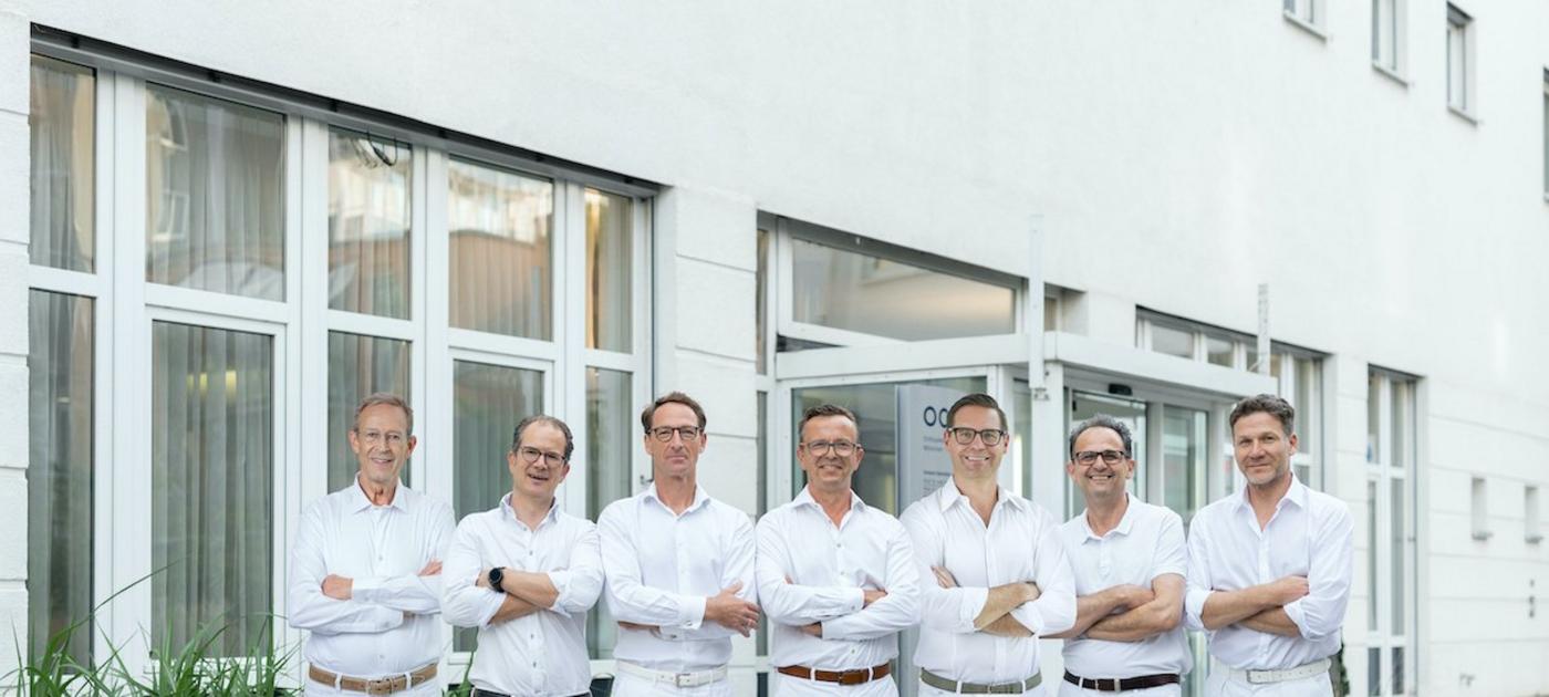 Endoprothetik-Team der OCM, 7 Ärzte in weiß, lächelnd, vor dem Eingang 