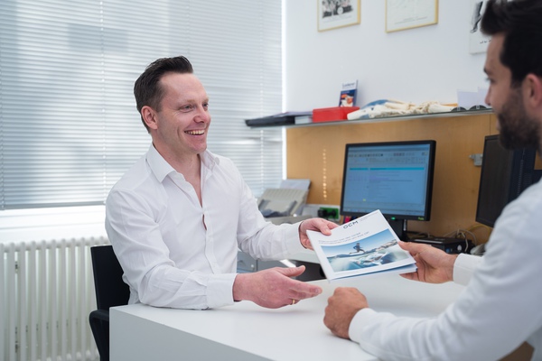 Arzt im Gespräch mit einem Patienten am Schreibtisch, beide sitzen und lächeln