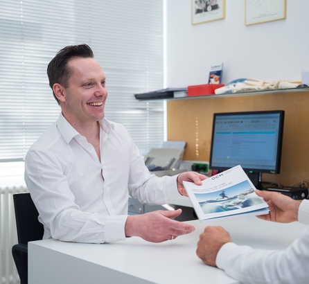Arzt im Gespräch mit einem Patienten am Schreibtisch, beide sitzen und lächeln