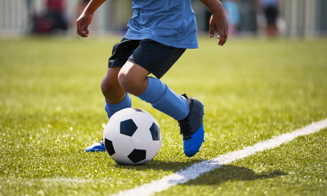 Kinderbeine mit Fußball auf dem Fußballplatz