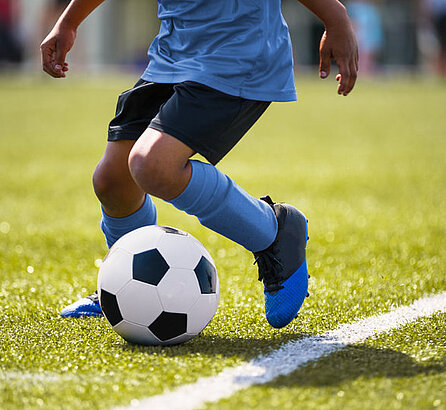 Kleiner Junge beim Fußballspielen auf einem grünen Rasen, Oberkörper nicht sichtbar