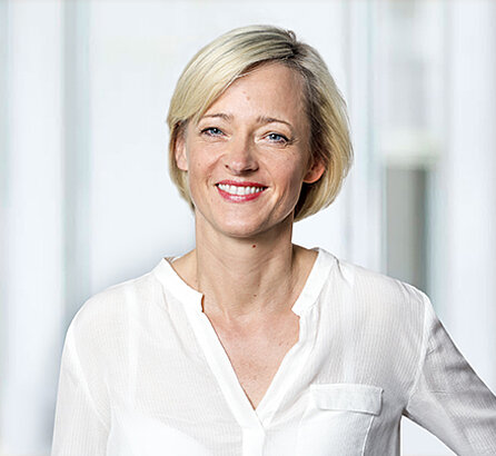 Portrait der OCM-Geschäftsführerin, blonde Frau in weißer Bluse, lächelnd