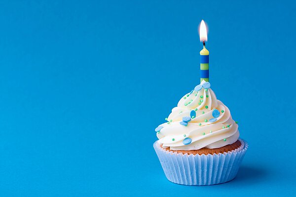 Cupcake mit einer Kerze vor blauem Hintergrund