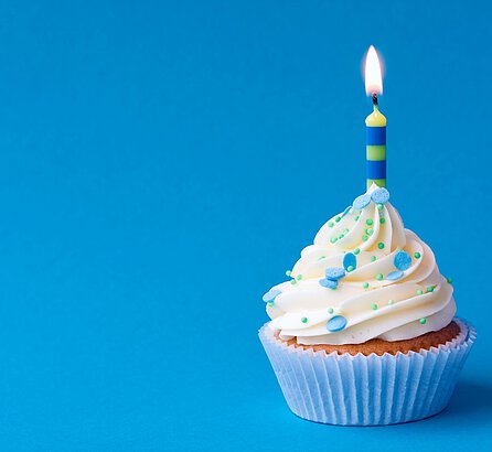 Cupcake mit einer Kerze vor blauem Hintergrund