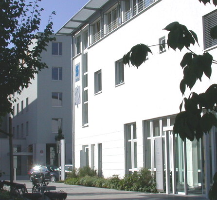 Seitenansicht des weißen OCM Gebäudes mit der Eingangstür, blauer Himmel, Sonnenschein