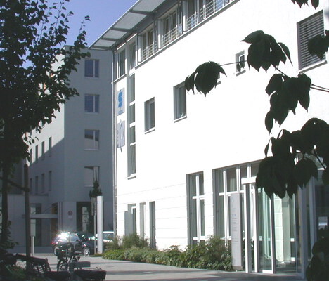 Seitenansicht des weißen OCM Gebäudes mit der Eingangstür, blauer Himmel, Sonnenschein
