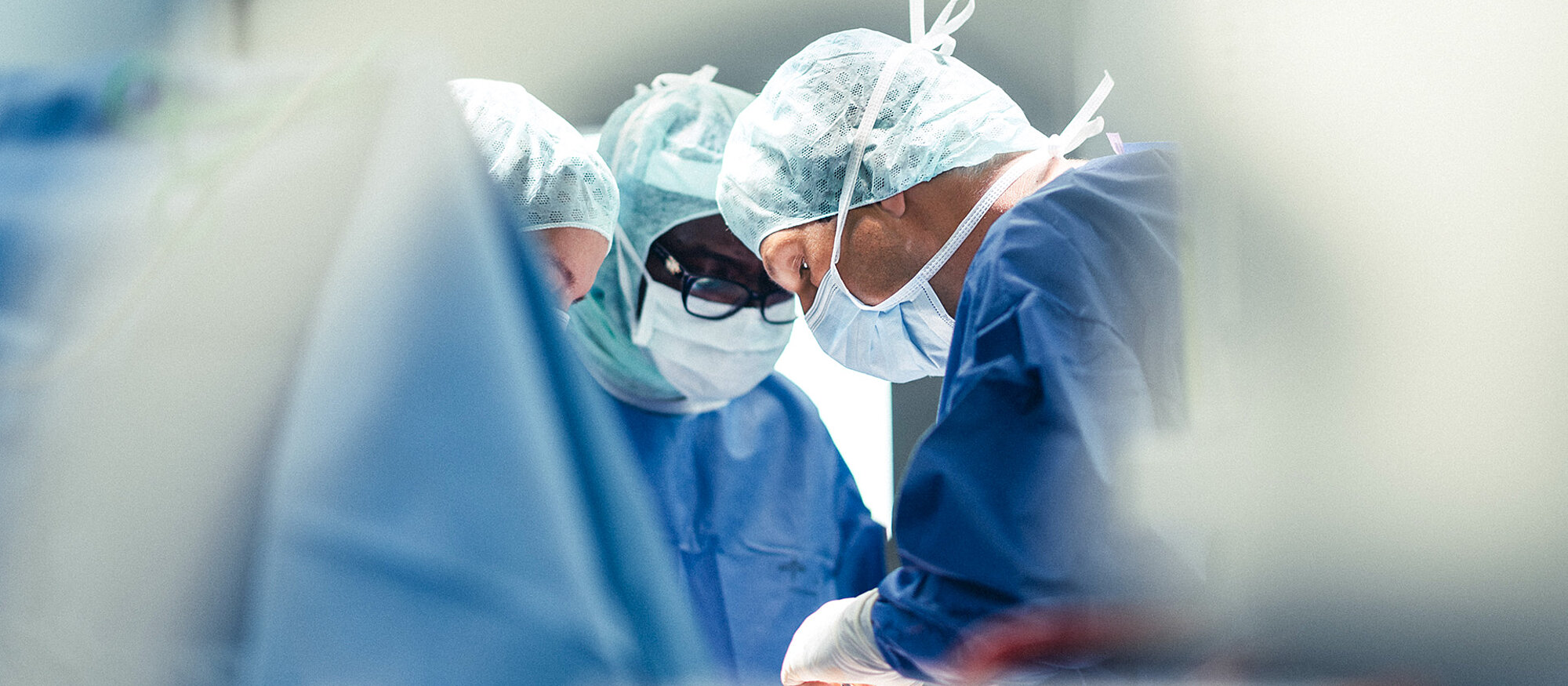 Ärzte im OP, Blautöne, Darstellung diffus, im Bild Banner "Den geeigneten Spezialisten finden", Button "Arzt finden"