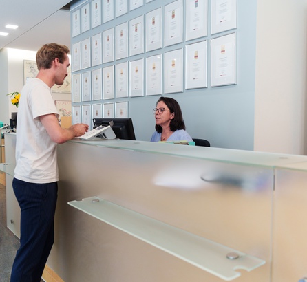 Empfang der Praxis OCM München, links im Bild ein stehender männlicher Patient, rechts eine sitzende Mitarbeiterin, beide im Gespräch miteinander