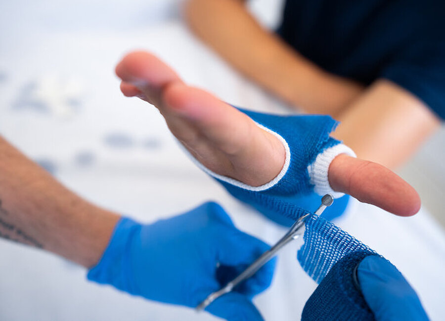 an der Hand eines Patienten wird ein Gipsverband angelegt, behandelnde Hände, Schere, Gips sichtbar